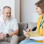 Caregiver taking notes with older man on sofa