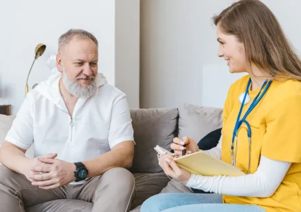 Caregiver taking notes with older man on sofa