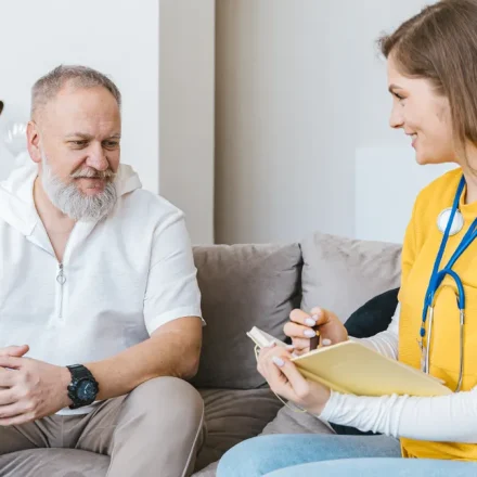 Caregiver taking notes with older man on sofa
