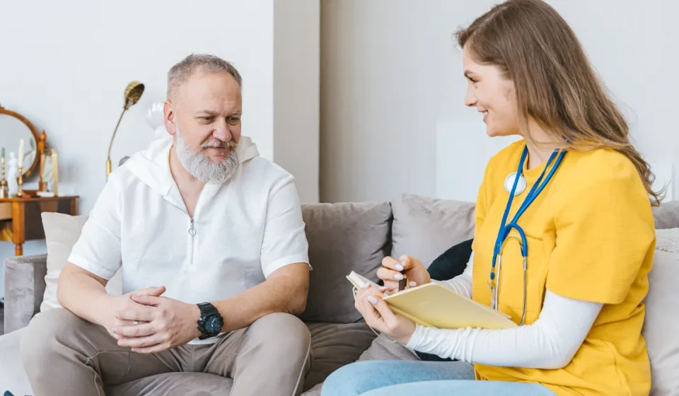 Caregiver taking notes with older man on sofa