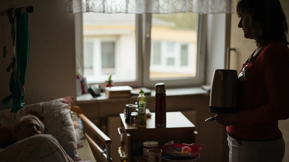 Dim bedroom with elderly person in bed and caregiver