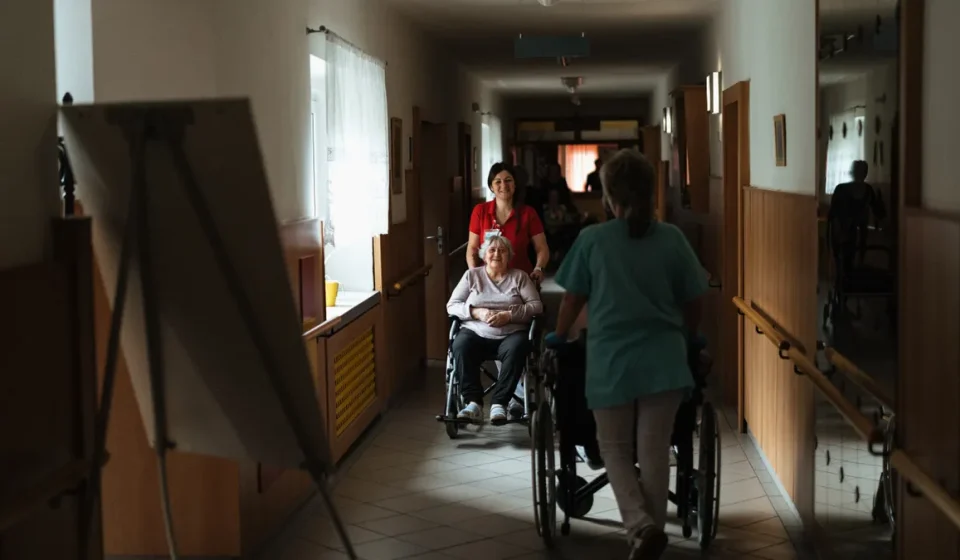 Caregiver pushing a wheelchair through a hallway