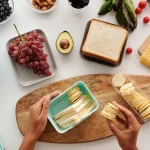 Hands arranging snack portions and sandwich pieces beside meal containers